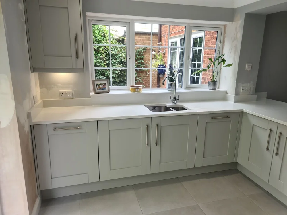 Sage green shaker kitchen with a white quartz worktop and a garden view over the sink